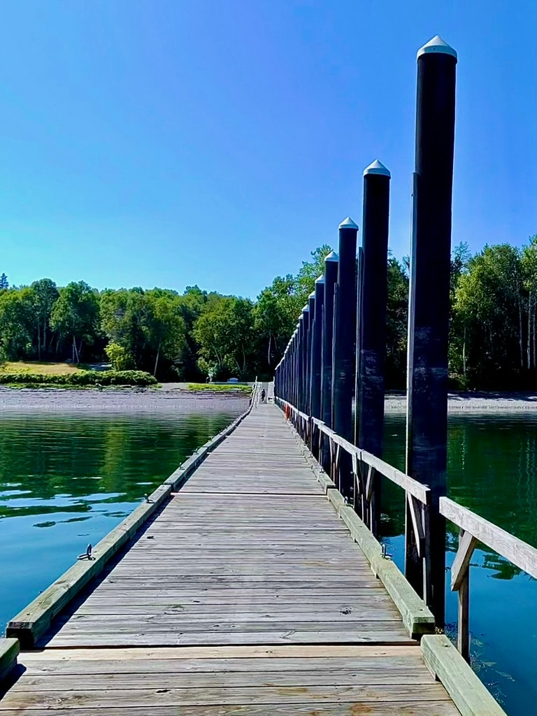 Wooden pier crossing calm water toward a tree-lined Campobello Island shore