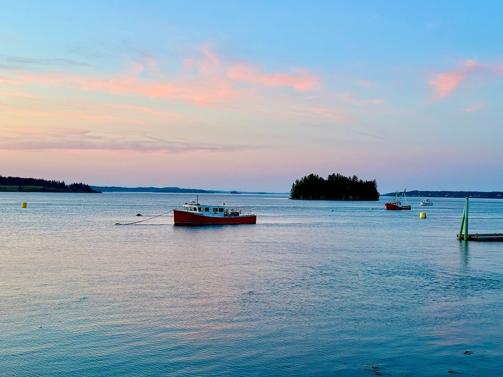Red fishing boat on calm coastal water beneath a pastel evening sky