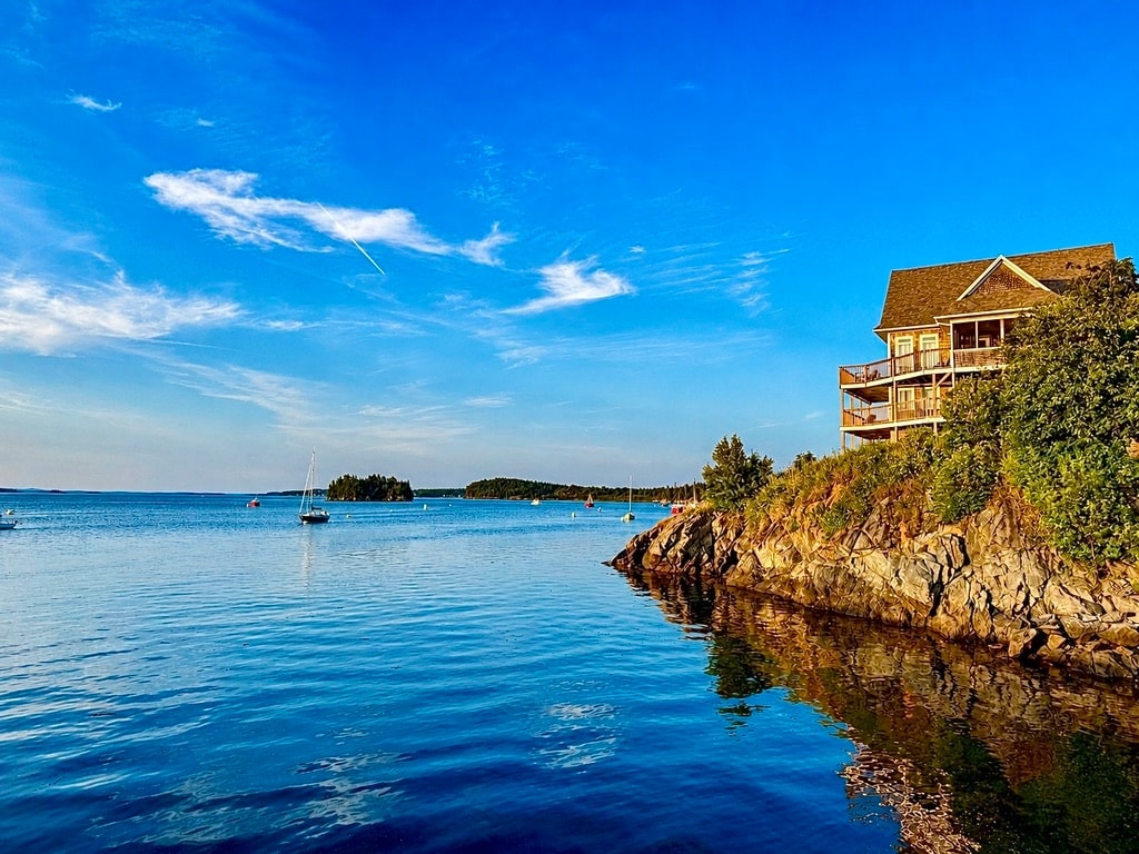 Waterfront home above calm blue water and sailboats in Lubec, Maine