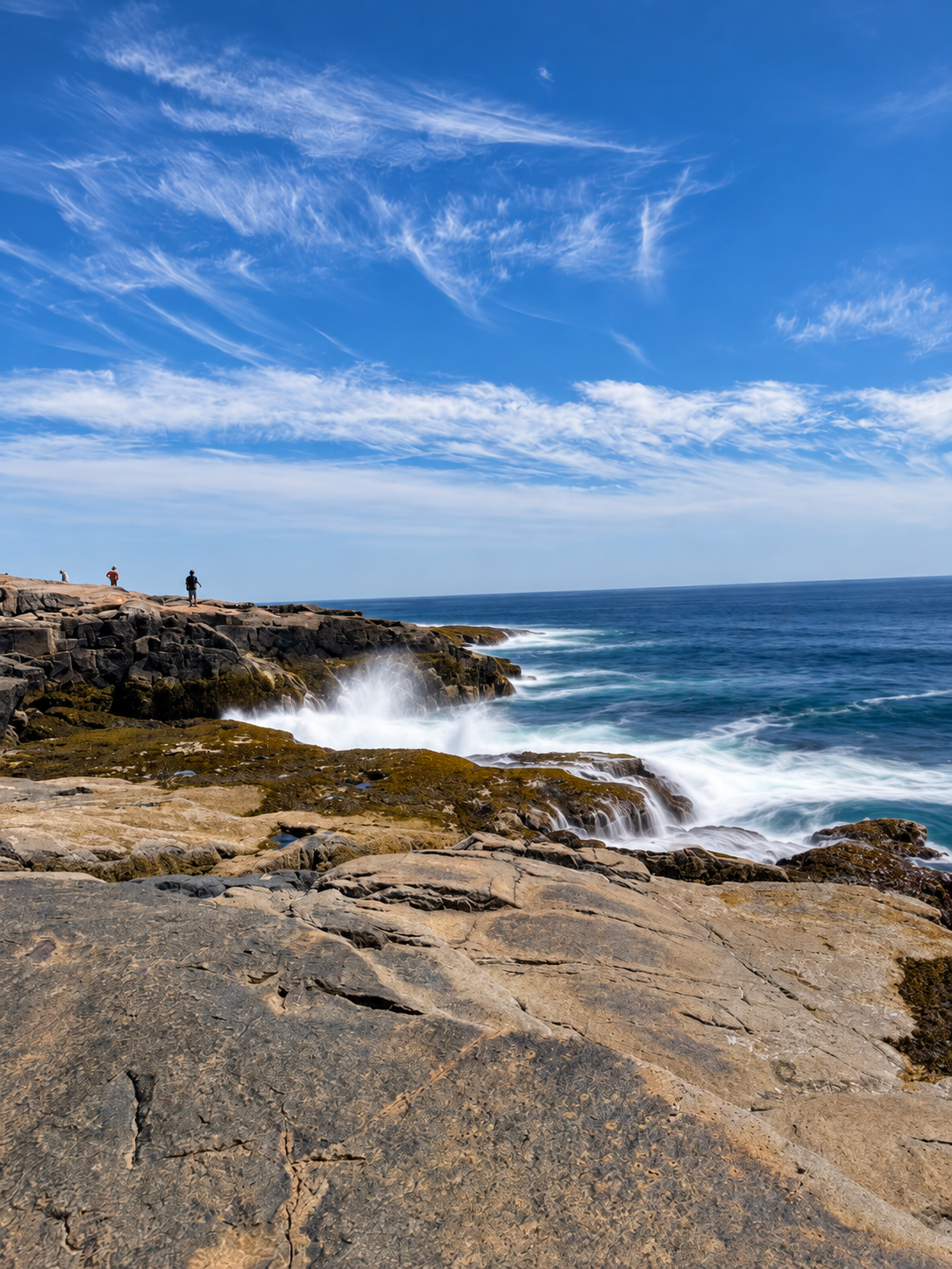 Waves breaking against the granite shoreline at Schoodic Point beneath a blue sky